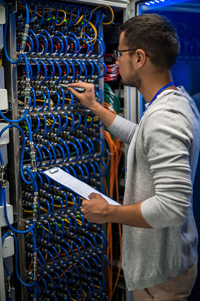 Back view portrait of young man connecting wires in server cabinet while working with supercomputer in data center